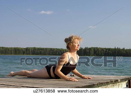 Stock Photo - 45 year old woman doing yoga on dock, no motors allowed on lake.; Canada, Manitoba, Riding Mountain National Park. Fotosearch