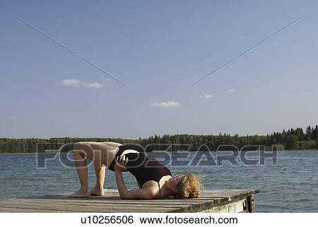Stock Photograph - 45 year old woman doing yoga on dock, no motors allowed on lake.; Canada, Manitoba, Riding Mountain National Park. Fotosearch