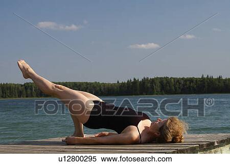 Stock Photography - 45 year old woman doing yoga on dock, no motors allowed on lake.; Canada, Manitoba, Riding Mountain National Park. Fotosearch