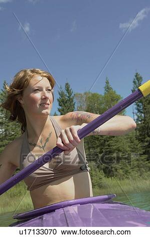 Stock Image - Woman paddles toward camera in purple kayak, Lake Katherine, Riding Mountain National Park, Manitoba, Canada. Fotosearch