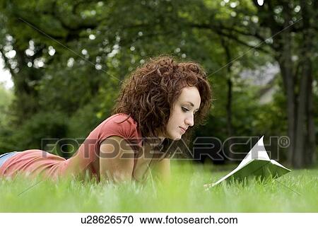 Stock Image - Woman reading book while lying on green grass, Winnipeg, Manitoba, Canada. Fotosearch