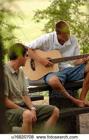 Stock Photo - Young guys playing guitar sitting at picnic table, Regina, Saskatchewan. Fotosearch
