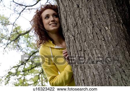 Stock Image - Young looks out from behind large tree, Munson Park, Winnipeg, Canada. Fotosearch