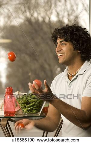 Stock Image - 20 year old man holding juggling organic tomatoes, Brandon, Manitoba, Canada. Fotosearch