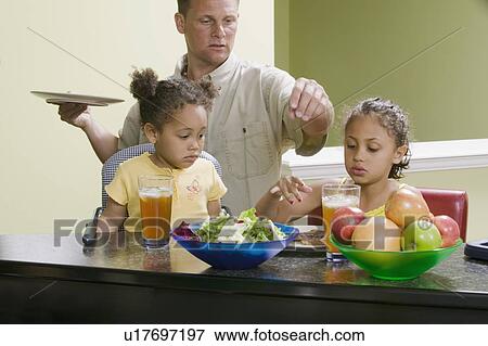 Stock Photo - Caucasian dad preparing a meal for his Mulatto children, girls 3 and 6 years.. Fotosearch