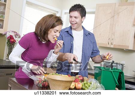 Stock Image - Couple cutting up fruit in kitchen, beside kitchen compost bin. Strawberrries container is made from compostable corn-based product, Winnipeg, Canada. Fotosearch