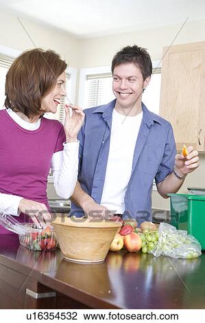 Stock Image - Couple cutting up fruit in kitchen, beside kitchen compost bin. Strawberrries container is made from compostable corn-based product, Winnipeg, Canada. Fotosearch