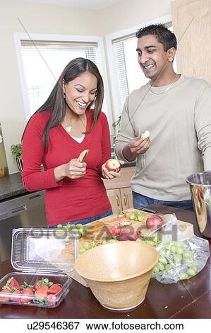 Stock Photo - Couple cutting up fruit in kitchen, beside kitchen compost bin. Strawberrries container is made from compostable corn-based product, Winnipeg, Canada. Fotosearch