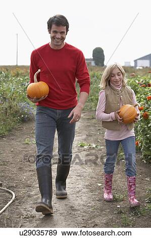 Stock Photo - Father and daughter with organic pumpkins walking in farm fields, Ladner, British Columbia. Fotosearch