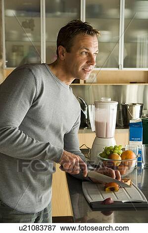 Stock Photo - Man cutting organic fruit for smoothie, Winnipeg, Canada. Fotosearch