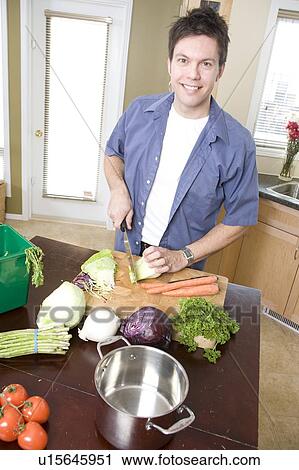 Stock Image - Man in kitchen cutting vegetables beside kitchen compost bin, Winnipeg, Canada. Fotosearch