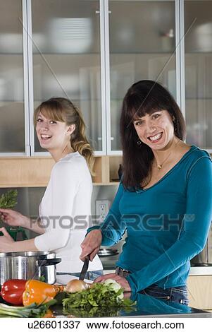 Stock Photo - Woman cutting vegetables, other woman puts vegetable scraps into kitchen compost pail, Winnipeg, Canada. Fotosearch