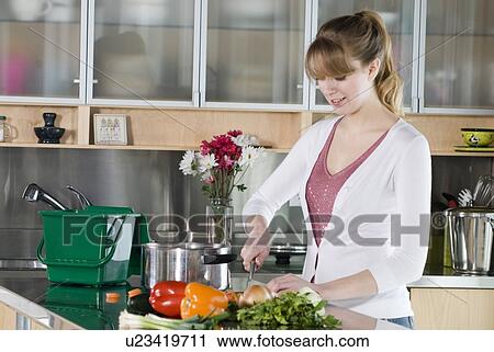 Stock Image - Woman cutting vegetables, with green kitchen compost pail for collecting kitchen scraps, Winnipeg, Canada. Fotosearch