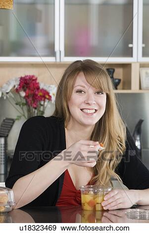 Stock Photo - Woman eating take out food from containers and spoon made from corn, and which are fully compostable, Winnipeg, Canada. Fotosearch
