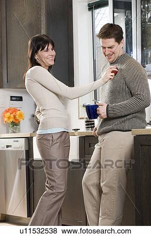 Stock Photo - Woman shines organic apple on man's sweater. Home has recovered/recycled cupboards and hardwood floors, Winnipeg, Canada. Fotosearch