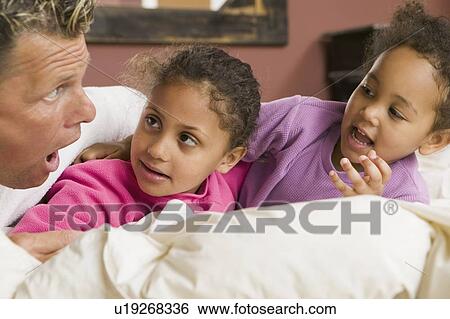 Stock Photograph - Caucasian dad and Mulatto daughters in bed (3 and 6 years old).. Fotosearch