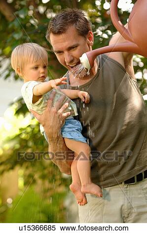 Stock Photography - Dad & baby playing with watering can, Regina, Saskatchewan. Fotosearch