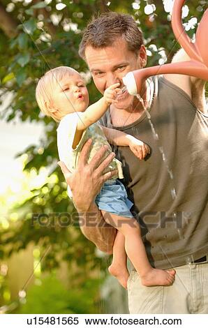 Stock Photography - Dad & baby playing with watering can, Regina, Saskatchewan. Fotosearch