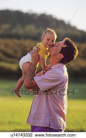 Stock Image - Dad kisses baby girl on cheek, she smiles, Kelowna, BC. Fotosearch