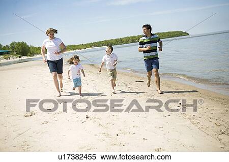 Stock Photography - Family of four running along shoreline, Grand Beach Provincial Park, Manitoba, Canada. Fotosearch