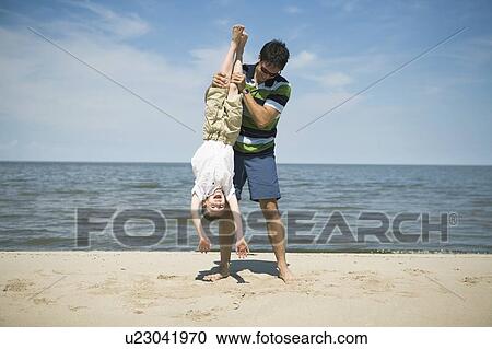 Stock Image - Man holds boy upside down, Grand Beach Provincial Park, Manitoba, Canada. Fotosearch