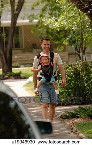 Stock Image - Man walking down street carrying baby in snuggly, Regina, Saskatchewan. Fotosearch