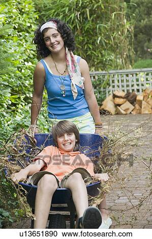 Stock Image - Teenage Siblings Playing With a Wheelbarrow. West Vancouver, BC.. Fotosearch