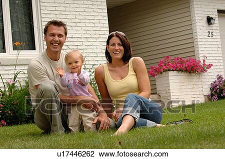 Stock Image - Young couple w/baby in front of house, Regina, Saskatchewan. Fotosearch