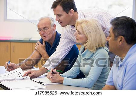 Stock Photography - Adult students in class with teacher helping (selective focus). Fotosearch