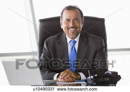 Stock Photo - Businessman in office with laptop smiling (high key/selective focus). Fotosearch