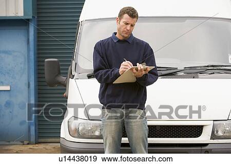 Stock Photo - Deliveryperson standing with van writing in clipboard. Fotosearch