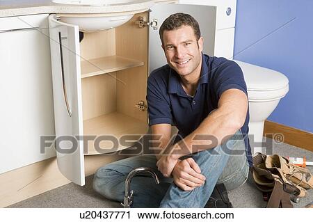 Stock Image - Plumber working on sink smiling. Fotosearch