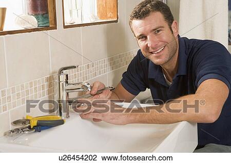 Stock Image - Plumber working on sink smiling. Fotosearch