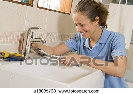 Stock Photo - Plumber working on sink smiling. Fotosearch
