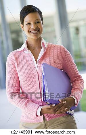 Teacher standing outside school holding binders and smiling (selective focus) View Large Photo Image Stock Image - Teacher standing outside school holding binders and smiling (selective focus). Fotosearch