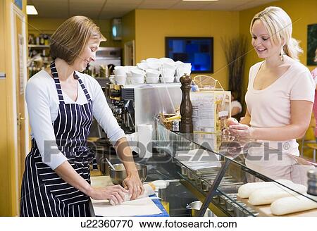 Stock Image - Woman standing at counter in restaurant serving customer smiling. Fotosearch