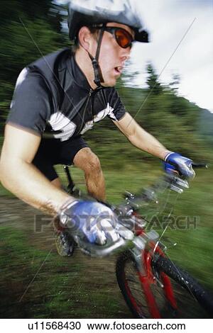 Stock Image - Man outdoors on trails riding bicycle (out of focus). Fotosearch