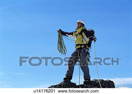 Stock Image - Mountain climber standing on top of mountain (selective focus). Fotosearch