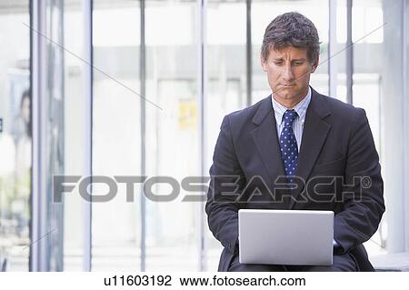 Businessman sitting in office lobby using laptop View Large Photo Image Stock Image - Businessman sitting in office lobby using laptop. Fotosearch