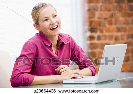 Stock Photograph - Businesswoman in office with laptop laughing. Fotosearch