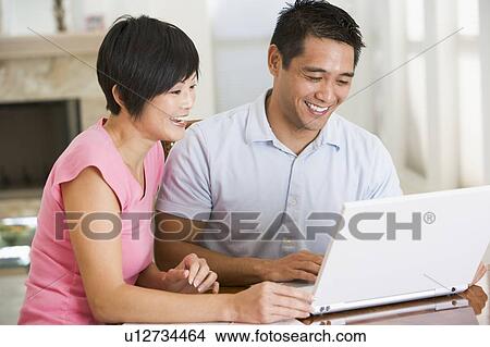 Picture - Couple in dining room with laptop smiling. Fotosearch