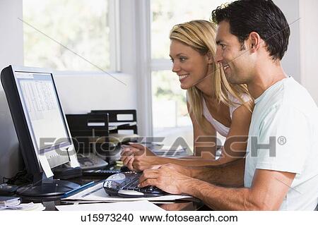 Stock Image - Couple in home office using computer and smiling. Fotosearch