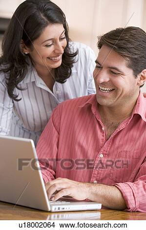 Picture - Couple in kitchen using laptop smiling. Fotosearch