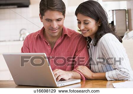 Stock Photo - Couple in kitchen with laptop smiling. Fotosearch