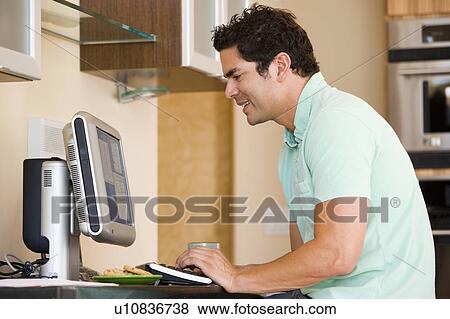 Man in kitchen using computer and smiling View Large Photo Image Stock Photo - Man in kitchen using computer and smiling. Fotosearch