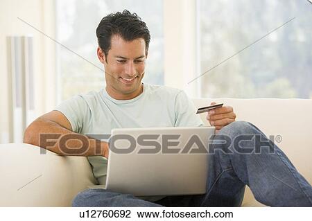 Man in living room using laptop and holding credit card smiling View Large Photo Image Stock Image - Man in living room using laptop and holding credit card smiling. Fotosearch