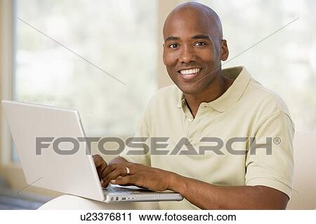 Man in living room using laptop and smiling View Large Photo Image Stock Image - Man in living room using laptop and smiling. Fotosearch