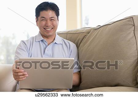 Stock Image - Man in living room using laptop and smiling. Fotosearch