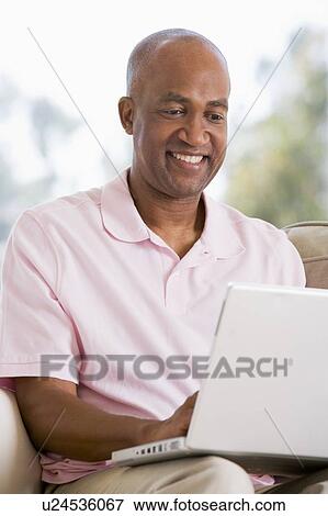 Stock Photo - Man in living room using laptop and smiling. Fotosearch