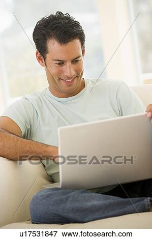 Stock Photo - Man in living room using laptop smiling. Fotosearch